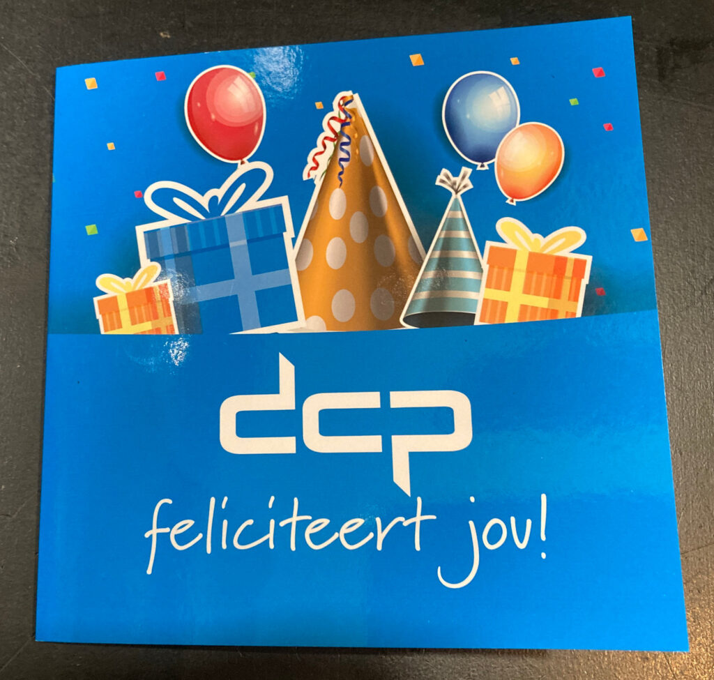 Front of postal card with party elements like party hat, presents and balloons and a text reading: "DCP Congratulates you!" in dutch